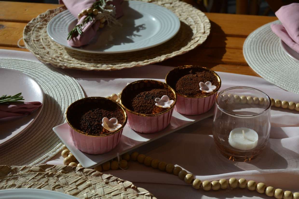 A table set with pink linen, woven placemats, wooden beads and individual desserts in gold-rimmed cases