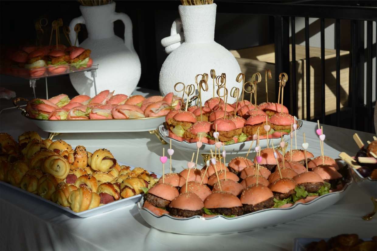 Tiered platters of sliders in pink brioche buns beside trays of savoury pastries